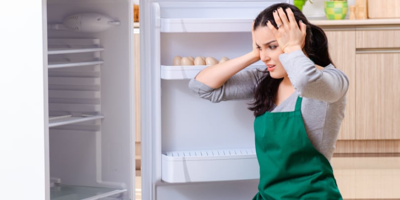 Eine Frau sitzt sorgenvoll vor ihrem defekten Kühlschrank